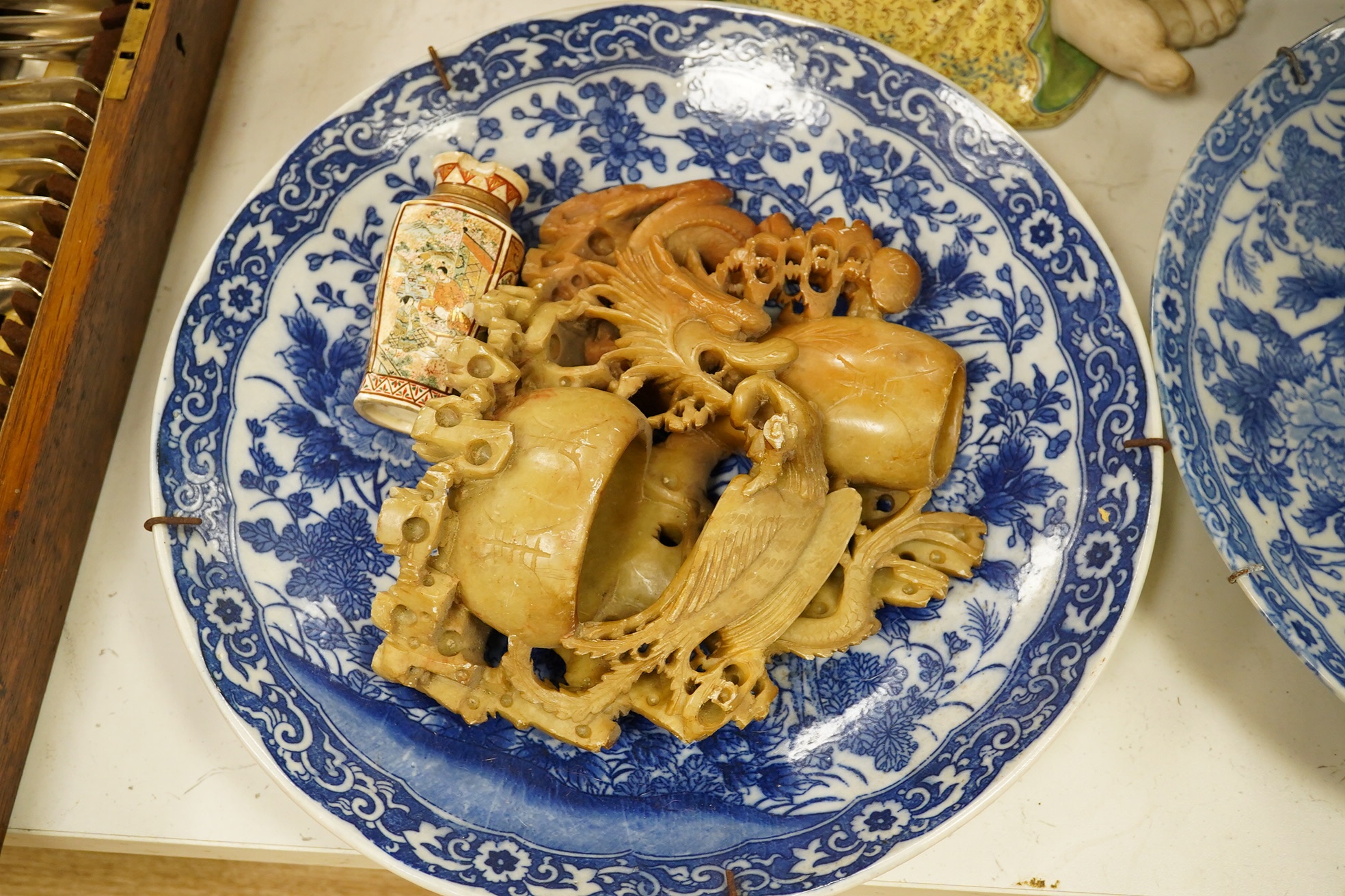 A collection of mostly Japanese and Chinese items including a floral hardstone flower in cloisonné pot, a hardstone carving of a Chinese Buddha and blue and white dishes. Condition - varies, fair